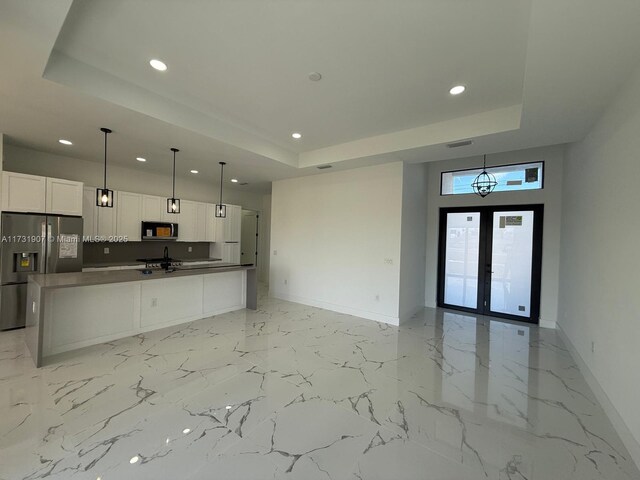 kitchen featuring pendant lighting, stainless steel fridge, a raised ceiling, and white cabinets