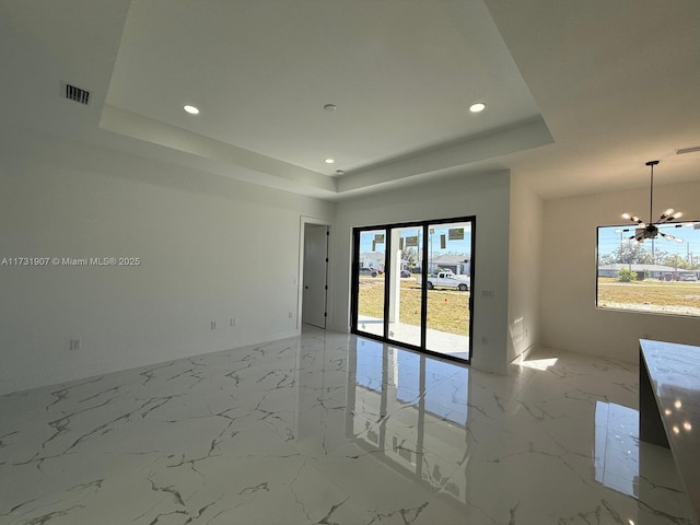 spare room with plenty of natural light, a tray ceiling, and a notable chandelier