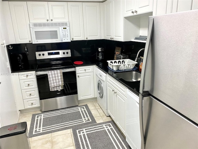 kitchen featuring washer / clothes dryer, white cabinetry, sink, light tile patterned floors, and white appliances