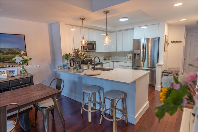 kitchen with sink, white cabinetry, hanging light fixtures, stainless steel appliances, and kitchen peninsula