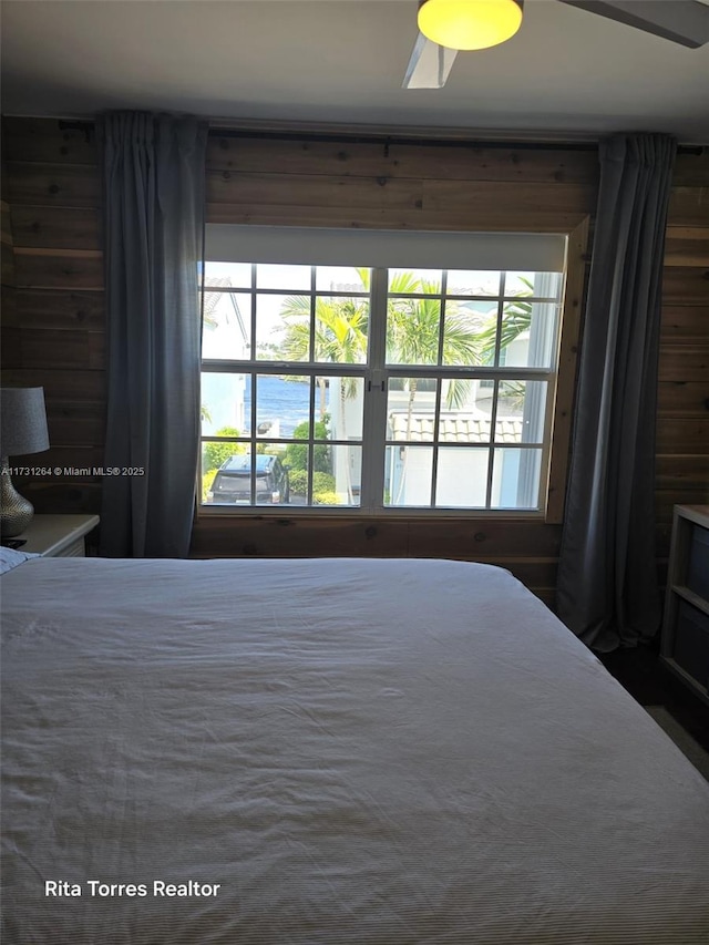 unfurnished bedroom with a water view, ceiling fan, and wood walls