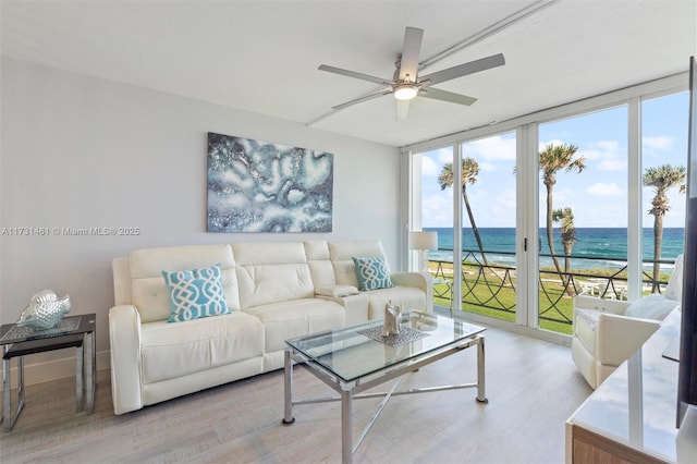 living room with expansive windows, a water view, a view of the beach, and ceiling fan