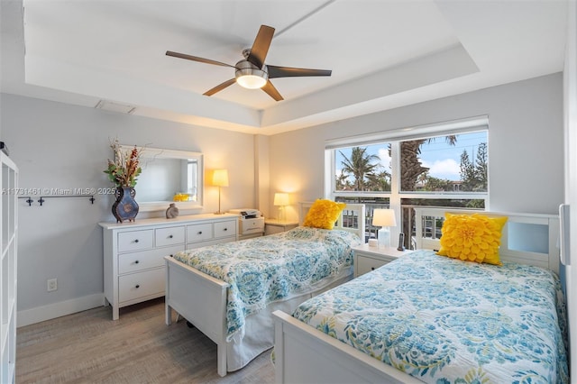 bedroom with a tray ceiling, light hardwood / wood-style flooring, and ceiling fan