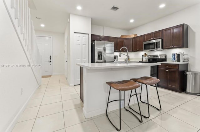 kitchen with an island with sink, sink, a kitchen breakfast bar, stainless steel appliances, and dark brown cabinets