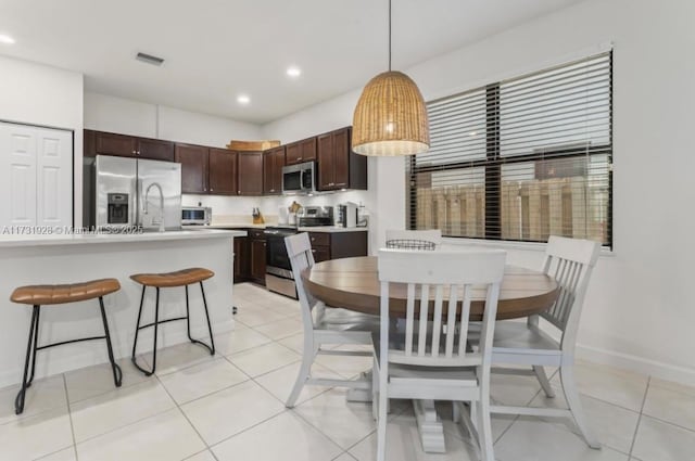 kitchen with pendant lighting, stainless steel appliances, dark brown cabinets, and light tile patterned floors