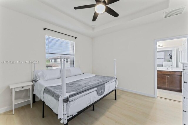 bedroom featuring connected bathroom, a raised ceiling, ceiling fan, and light wood-type flooring