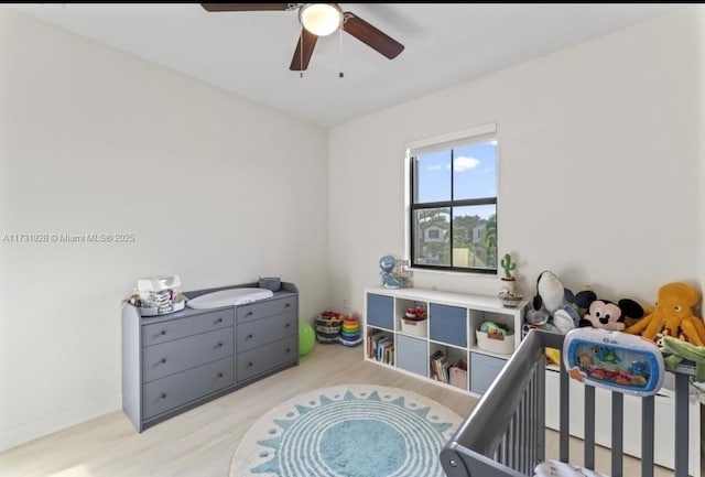 bedroom with light hardwood / wood-style flooring, a nursery area, and ceiling fan