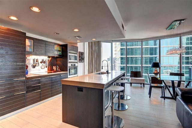 kitchen featuring sink, a wall of windows, a kitchen island with sink, stainless steel appliances, and a kitchen bar