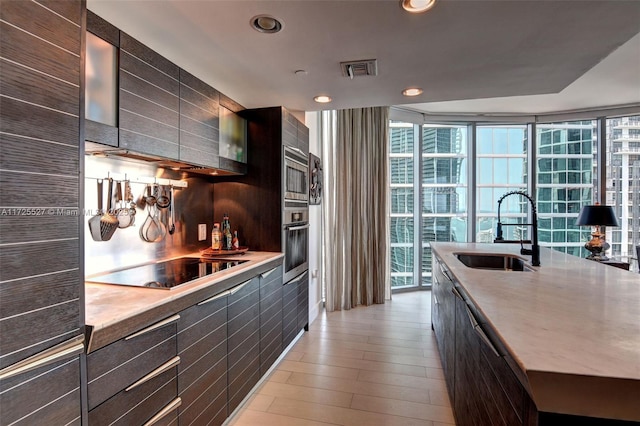 kitchen featuring floor to ceiling windows, sink, appliances with stainless steel finishes, a kitchen island with sink, and light hardwood / wood-style floors