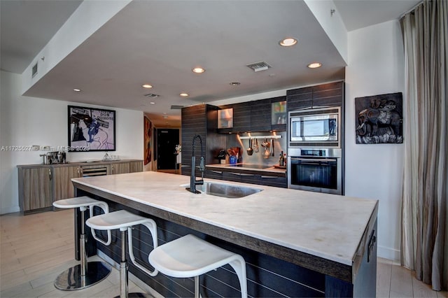 kitchen with sink, a kitchen bar, stainless steel appliances, a center island with sink, and light hardwood / wood-style flooring