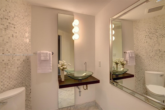 bathroom featuring toilet, sink, and tile walls