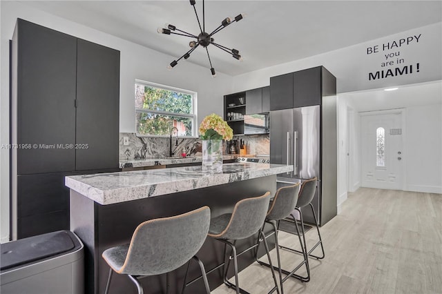 kitchen with high quality fridge, sink, light hardwood / wood-style floors, and a breakfast bar area