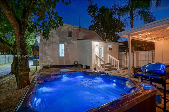 pool at night featuring a hot tub