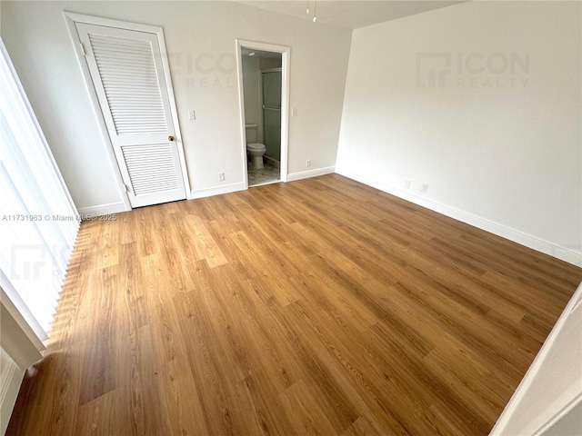 unfurnished bedroom with ensuite bathroom and light wood-type flooring