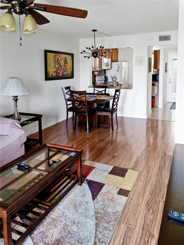 living room with hardwood / wood-style floors, ceiling fan with notable chandelier, and a textured ceiling