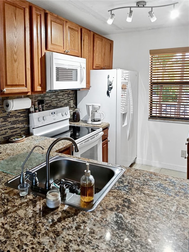 kitchen featuring sink, white appliances, rail lighting, dark stone countertops, and decorative backsplash