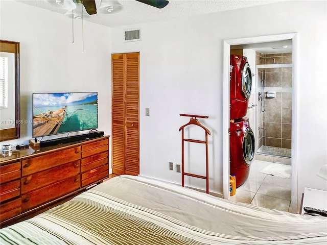 bedroom with ceiling fan, stacked washing maching and dryer, connected bathroom, a textured ceiling, and light tile patterned flooring