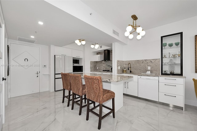 kitchen featuring a kitchen bar, decorative light fixtures, a center island, white appliances, and white cabinets