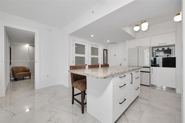 kitchen featuring a breakfast bar area, a center island, light stone countertops, white cabinets, and white fridge