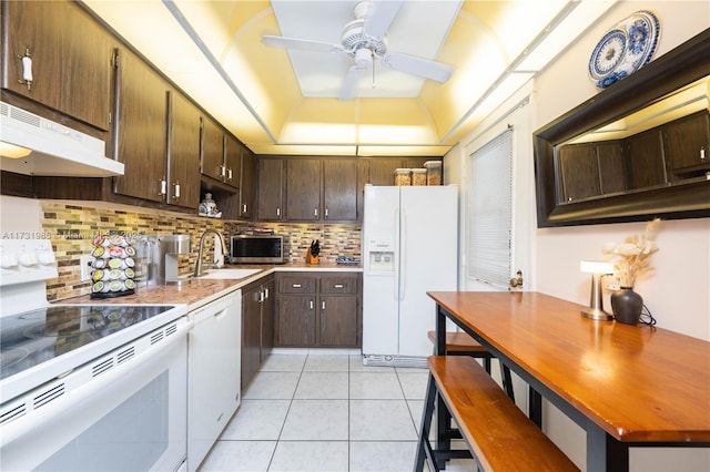 kitchen featuring light tile patterned flooring, sink, decorative backsplash, a tray ceiling, and white appliances