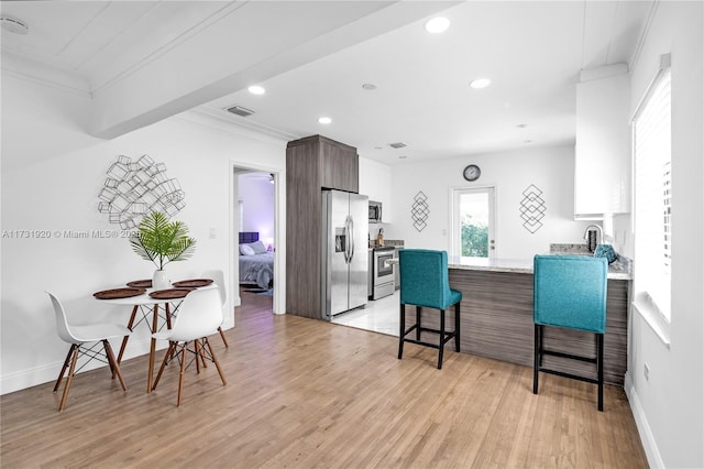 kitchen featuring appliances with stainless steel finishes, a kitchen bar, ornamental molding, light hardwood / wood-style floors, and kitchen peninsula