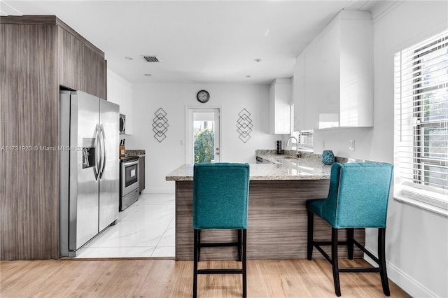 kitchen with sink, appliances with stainless steel finishes, white cabinetry, light stone countertops, and a kitchen bar