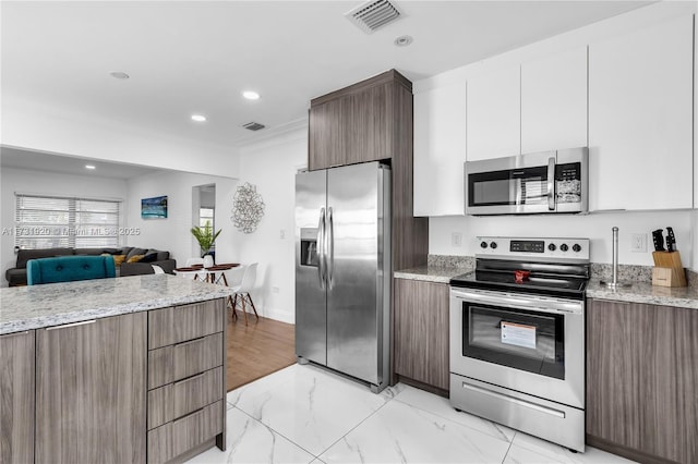 kitchen featuring white cabinetry, ornamental molding, appliances with stainless steel finishes, and light stone countertops