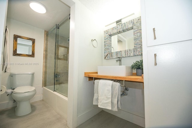 full bathroom with hardwood / wood-style flooring, sink, shower / bath combination with glass door, and toilet