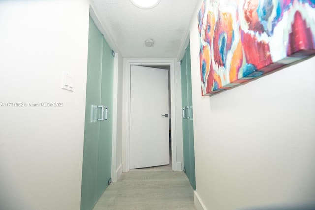 hall with a textured ceiling and light wood-type flooring