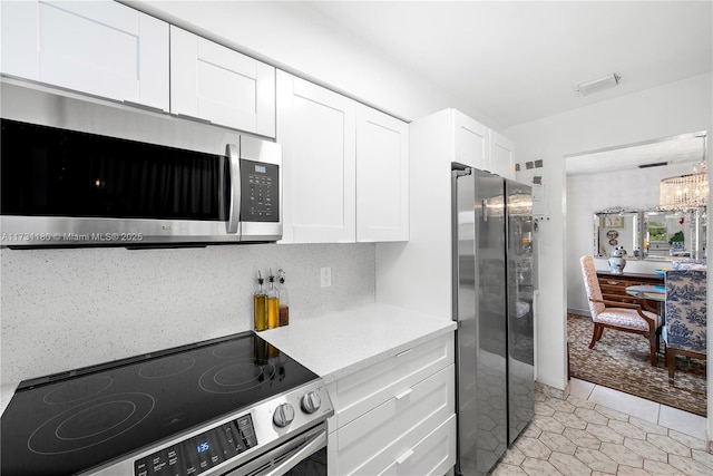 kitchen featuring light tile patterned floors, appliances with stainless steel finishes, tasteful backsplash, white cabinets, and a chandelier