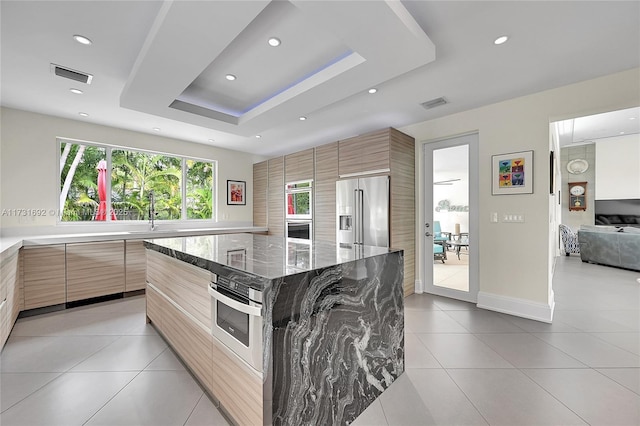 kitchen featuring a large island, stainless steel appliances, light stone counters, a tray ceiling, and light tile patterned flooring