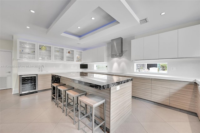 kitchen featuring wine cooler, a breakfast bar area, white cabinetry, a tray ceiling, and a kitchen island