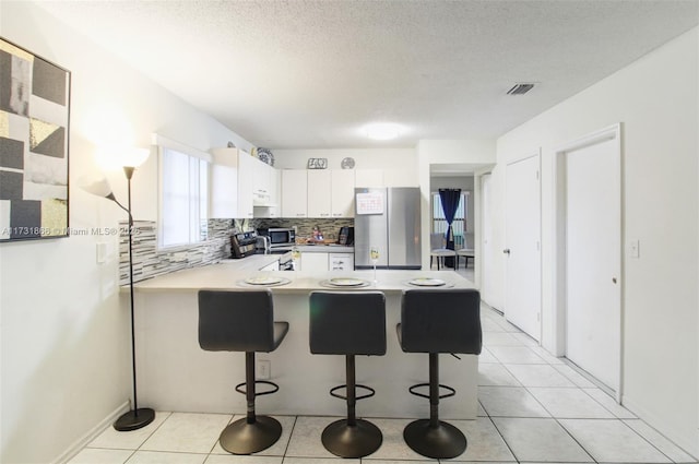 kitchen with light tile patterned floors, white cabinetry, stainless steel appliances, a kitchen breakfast bar, and kitchen peninsula