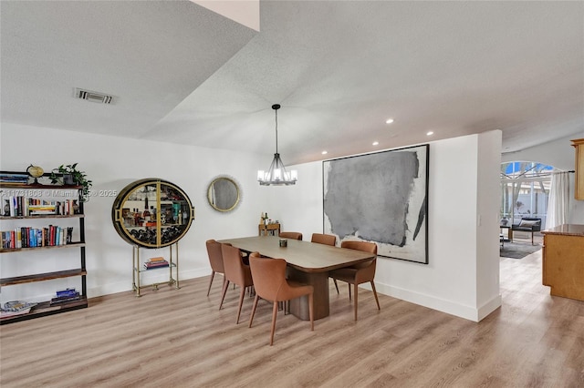 dining space with light hardwood / wood-style flooring, a chandelier, and a textured ceiling