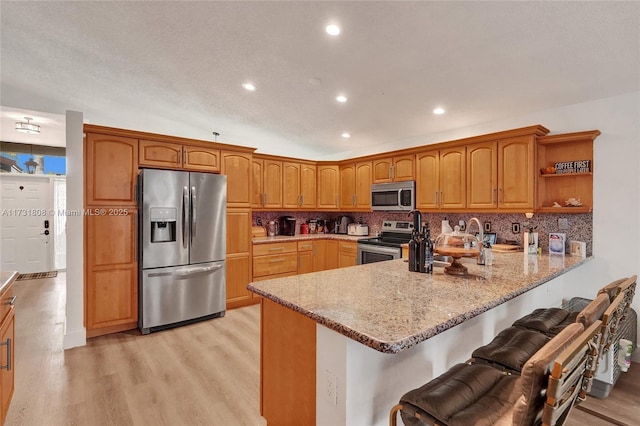 kitchen with sink, light stone counters, light wood-type flooring, kitchen peninsula, and stainless steel appliances