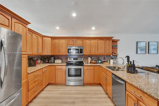 kitchen with light stone counters, appliances with stainless steel finishes, sink, and light wood-type flooring