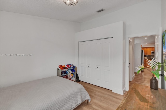 bedroom featuring stainless steel refrigerator, a textured ceiling, a closet, and light hardwood / wood-style flooring