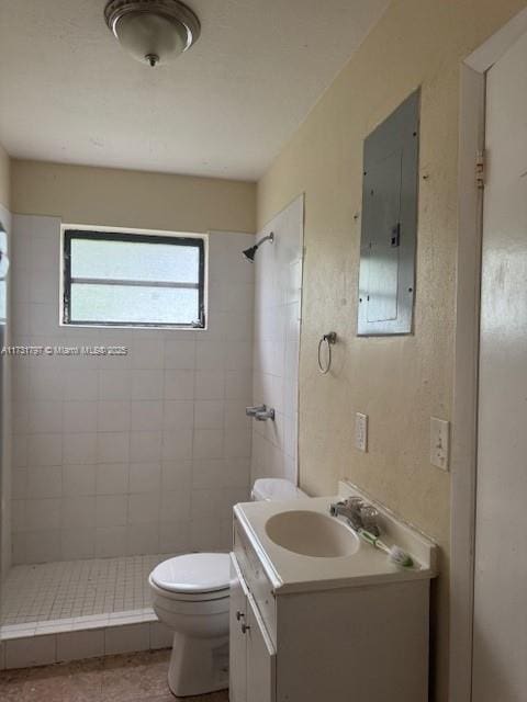 bathroom with vanity, a tile shower, electric panel, and toilet