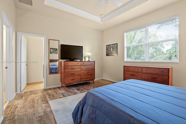 bedroom featuring crown molding, light hardwood / wood-style flooring, ceiling fan, and a tray ceiling