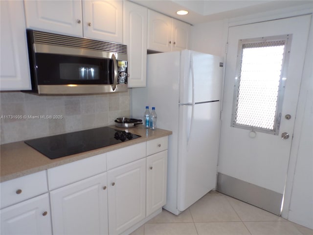 kitchen featuring light tile patterned flooring, white cabinetry, decorative backsplash, white refrigerator, and black electric cooktop