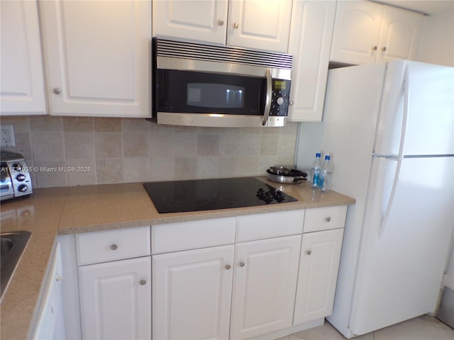 kitchen with light tile patterned flooring, white fridge, black electric stovetop, decorative backsplash, and white cabinets