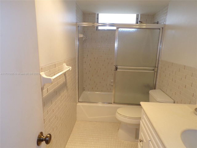 full bathroom featuring combined bath / shower with glass door, tile walls, tile patterned flooring, vanity, and toilet