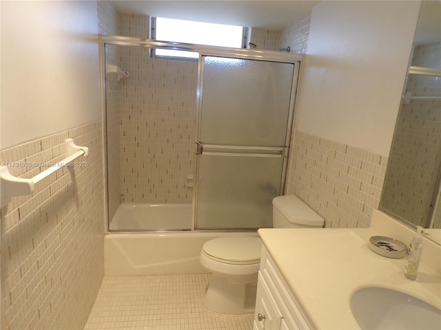 full bathroom featuring tile patterned floors, toilet, combined bath / shower with glass door, tile walls, and vanity