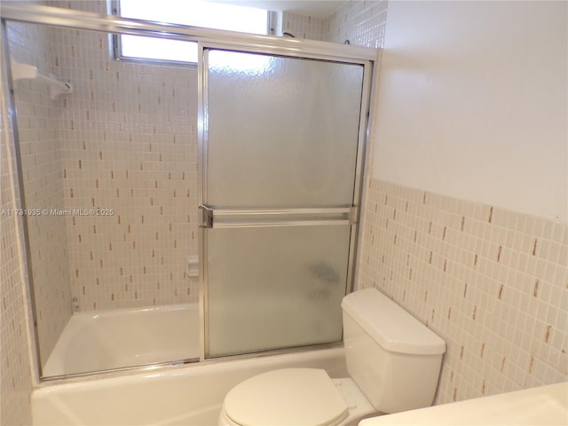 bathroom featuring tile walls, toilet, and combined bath / shower with glass door