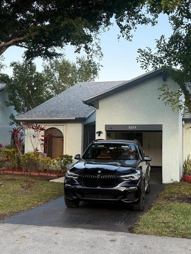 view of front of home featuring a shingled roof, an attached garage, and stucco siding