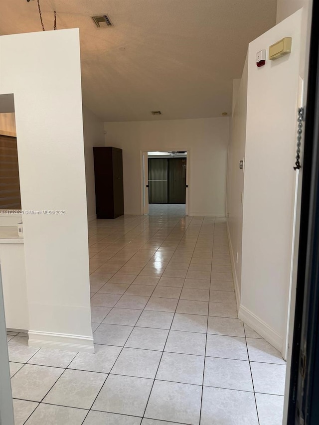 corridor featuring light tile patterned floors, baseboards, and visible vents