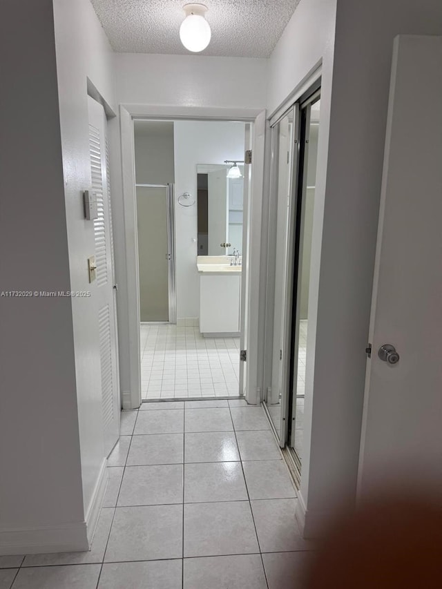 corridor featuring a textured ceiling, baseboards, and light tile patterned floors