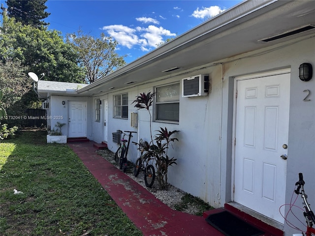 view of exterior entry featuring a wall mounted air conditioner and a lawn