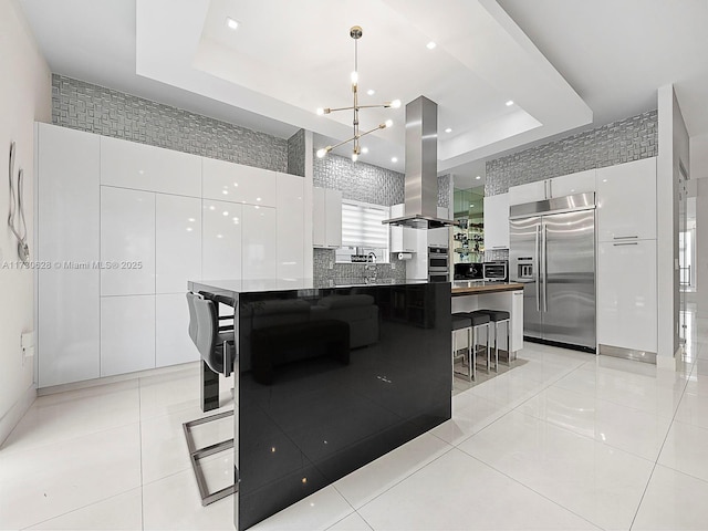 kitchen featuring white cabinetry, island exhaust hood, appliances with stainless steel finishes, and a tray ceiling