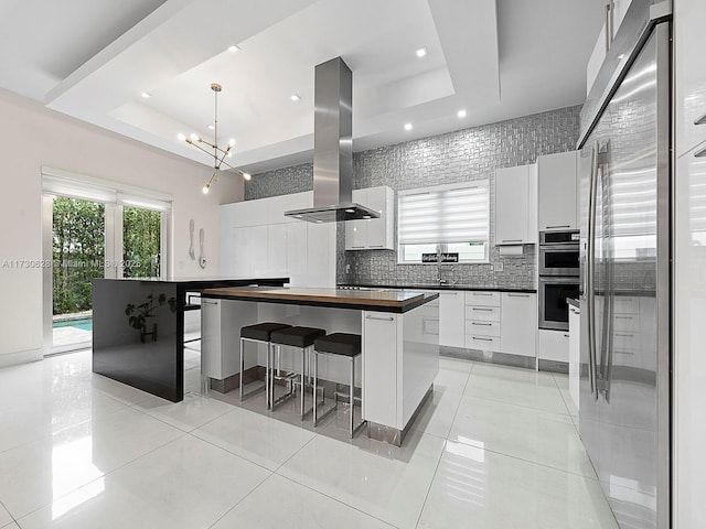 kitchen with a tray ceiling, island exhaust hood, white cabinets, and a kitchen island